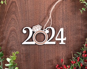 May include: White wooden ornament shaped like the numbers 2024 with a brown ring and diamond design in the center. The ornament is hanging from a string.