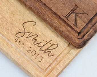 May include: Personalized wooden cutting board with a raised edge and a custom engraved design. The board features the text "Smith est. 2013" and the initial "K" in a script font.