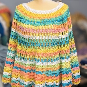 Może przedstawiać: Kolorowy ponczo zrobiony na szydełku w paski w kolorze białym, żółtym, pomarańczowym, różowym, zielonym i niebieskim.