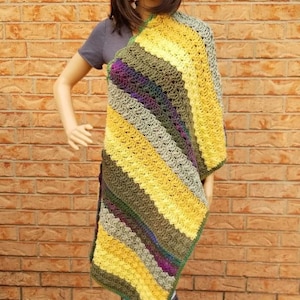 May include: A crocheted shawl with stripes of yellow, green, and purple yarn. The shawl is draped over a mannequin.