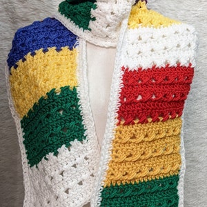 May include: A colorful crocheted scarf with stripes of white, yellow, green, red, and blue. The scarf is made with a variety of stitches and is finished with a white border.