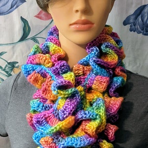 May include: A colorful crocheted scarf with a rainbow pattern. The scarf is made of yarn in shades of pink, purple, blue, green, yellow, and orange.