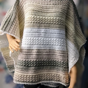 May include: A crocheted poncho with a multi-colored ombre design in shades of beige, brown, and white. The poncho has a wide, open neckline and a loose, flowing fit.