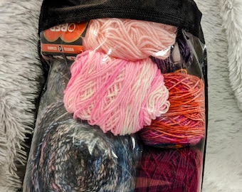 May include: A black mesh bag with a clear plastic window containing five balls of yarn in various colors, including pink, red, white, and blue.