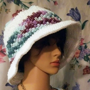 May include: White crochet sun hat with stripes of purple, green, and blue. The hat is wide-brimmed and has a floppy shape.