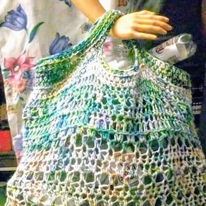 May include: A crocheted green, blue, and white string bag with a white background. The bag is filled with plastic bottles.