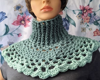 May include: A crocheted cowl with a green ombre design. The cowl is made with a thick yarn and has a scalloped edge.