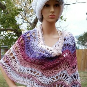 May include: A crocheted poncho with a multi-colored ombre design in shades of pink, purple, and white. The poncho has a wide, open neckline and a loose, flowing fit. The model is wearing a white and gray crocheted hat.