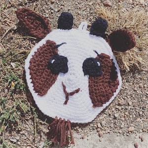 May include: A white crocheted animal with brown ears and patches around the eyes. The animal has a black nose and a stitched-on smile.