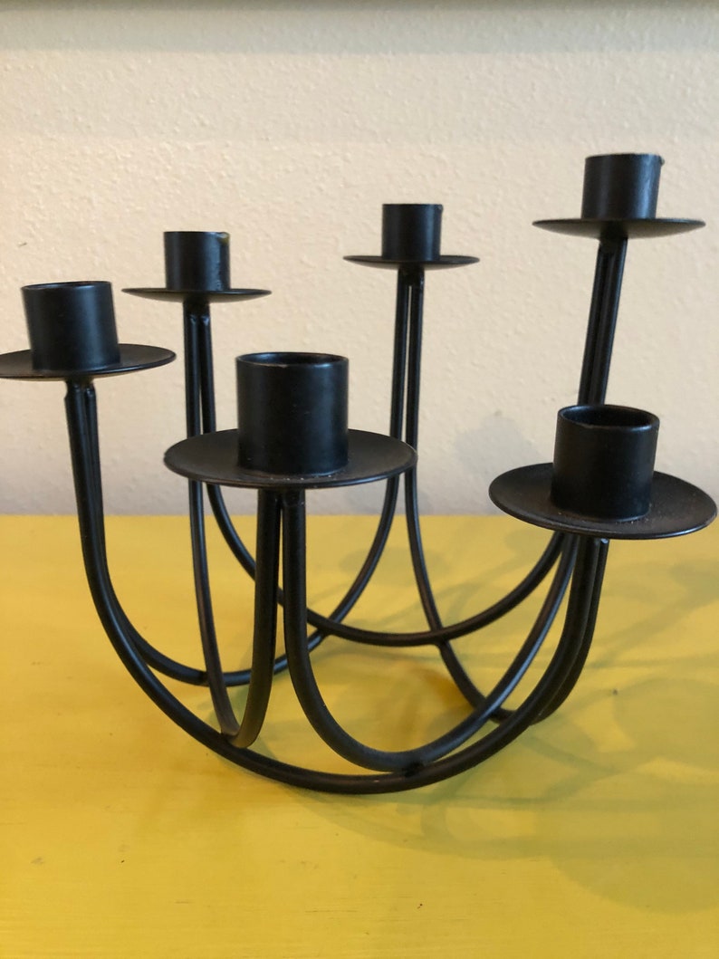 Puede incluir: Un candelabro de metal negro con seis portavelas. Los soportes son circulares y se asientan sobre brazos delgados y curvos. La base es una serie de arcos interconectados. El candelabro est&aacute; dise&ntilde;ado para sostener m&uacute;ltiples velas.
