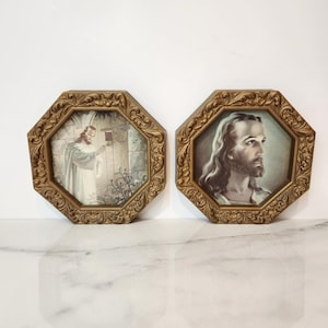 May include: Two framed religious prints. Each print is octagonal with a gold-colored, ornate frame. One print depicts a figure in white robes at a doorway. The other print shows a portrait of a man with long hair and a beard.