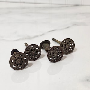 May include: A set of four round metal drawer knobs featuring an intricate openwork filigree pattern. Each knob has a dark, weathered bronze-toned finish and includes a threaded metal post extending from the back for mounting purposes.