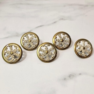 May include: Five circular buttons featuring a metallic gold outer rim and a central openwork design with white filigree patterns. Each button has a raised gold center point surrounded by symmetrical, curved white metal scrollwork details.