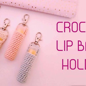 Peut inclure: Quatre porte-baume à lèvres en crochet de couleur rose, beige, rose clair et gris avec des porte-clés argentés. Les porte-baume sont sur un fond rose avec le texte "CROCHET LIP BALM HOLDER" en rose.