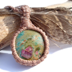 Puede incluir: Un collar de cordón de cuero marrón con un colgante redondo de piedra preciosa verde, rosa y blanca.