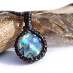 May include: A brown leather cord necklace with a round abalone shell pendant. The shell has iridescent blue, green, and purple colours.