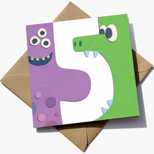 May include: A birthday card featuring the number five, split into purple and green sections. The purple section has a monster face, and the green section has a monster face. The card rests on a brown envelope.