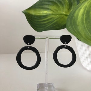 May include: A pair of black clay hoop earrings with a small black clay circle on top of each hoop.