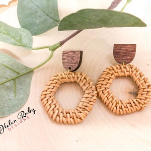 Peut inclure: Une paire de boucles d'oreilles en bois tressé avec un accent en bois brun. Les boucles d'oreilles sont de couleur brun clair et ont une texture tressée. Les boucles d'oreilles sont suspendues à une surface en bois.
