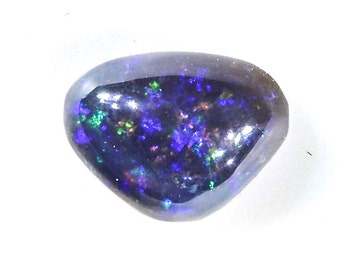 May include: A polished, dark opal gemstone with a rounded triangular shape. The stone displays a vibrant play-of-colour, with flashes of blue, green, and purple against a dark background. The opal is set against a white background.