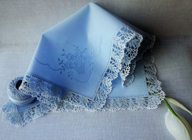 May include: A light blue handkerchief with a delicate floral embroidery design and a white crocheted lace border.