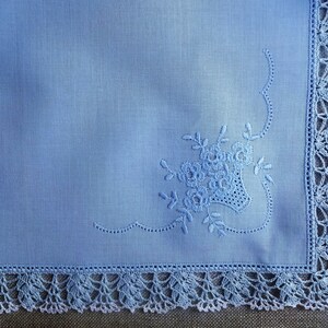 May include: A light blue linen handkerchief with a delicate floral embroidery design and a crocheted border.