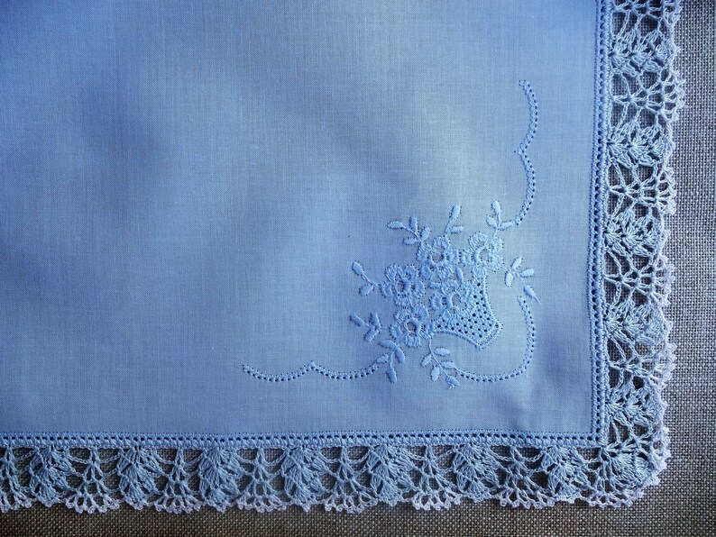 May include: A light blue linen handkerchief with a delicate floral embroidery design and a crocheted border.