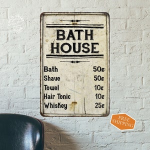 May include: Vintage-style metal sign with the text "Bath House" and a price list for various services, including bath, shave, towel, hair tonic, and whiskey. The sign has a distressed, aged look and is painted in black and white.