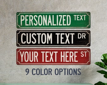 May include: Three personalized street signs with different colors and text. The top sign is green with white text that says "PERSONALIZED TEXT". The middle sign is black with white text that says "CUSTOM TEXT DR". The bottom sign is red with white text that says "YOUR TEXT HERE ST". Below the signs is the text "9 COLOR OPTIONS".