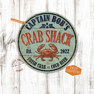 May include: A round, blue and white sign with the text "Captain Bob's Crab Shack" in a vintage style font. The sign also includes a drawing of a crab, the text "Est. 2022", and the phrase "Fresh Crab - Cold Beer".