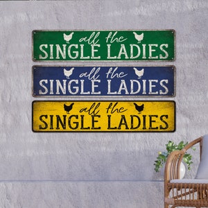 Pu&ograve; includere: Tre cartelli in legno rustico con una finitura usurata. Ogni cartello presenta una silhouette di pollo bianca e il testo "all the single ladies" in lettere nere. I cartelli sono dipinti in verde, blu e giallo.