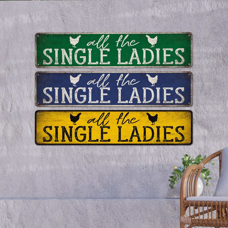 Pu&ograve; includere: Tre cartelli in legno rustico con una finitura usurata. Ogni cartello presenta una silhouette di pollo bianca e il testo "all the single ladies" in lettere nere. I cartelli sono dipinti in verde, blu e giallo.