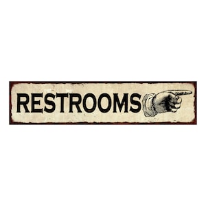 May include: A vintage-style metal sign with a distressed, cream-colored background and a black border. The sign reads "RESTROOMS" in black block letters with a black and white illustration of a hand pointing to the right.