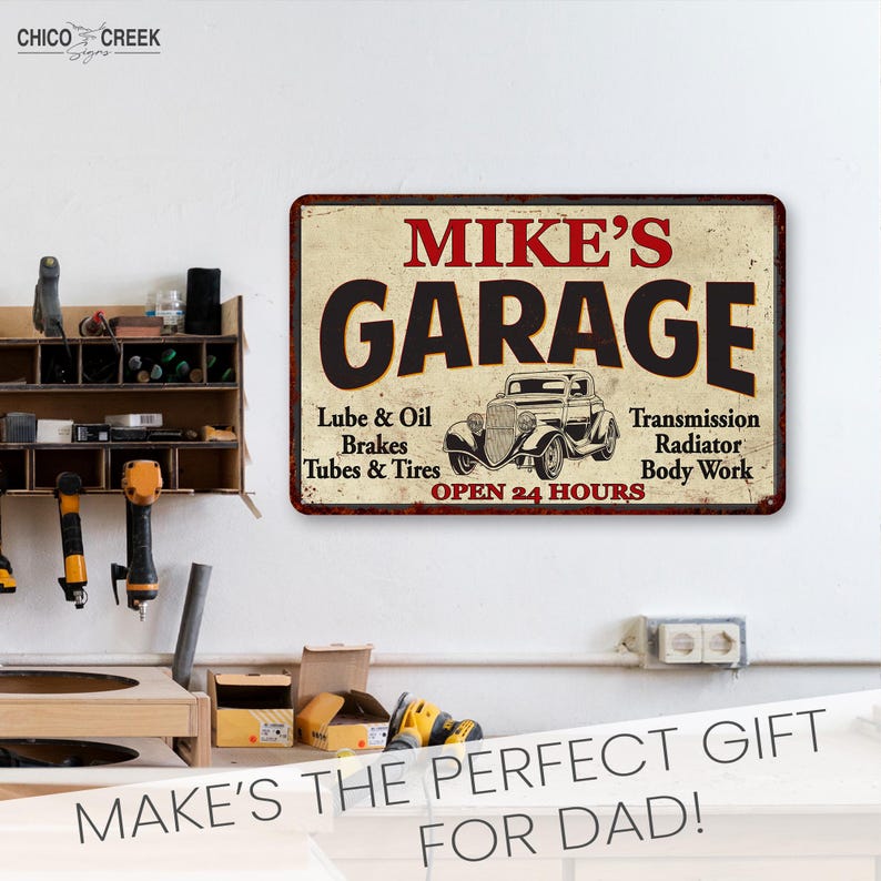 May include: A vintage-style metal sign with the text "MIKE'S GARAGE" in black lettering on a cream background. The sign features a black and white illustration of a classic car and the text "Lube & Oil, Brakes, Tubes & Tires, Transmission, Radiator, Body Work, OPEN 24 HOURS" in red lettering.