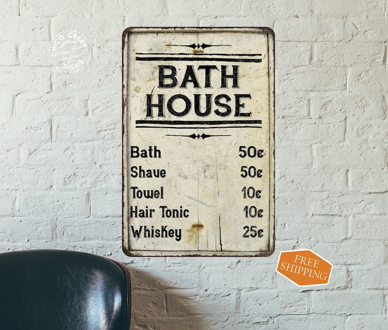 May include: Vintage-style metal sign with the text "Bath House" and a price list for various services, including bath, shave, towel, hair tonic, and whiskey. The sign has a distressed, aged look and is painted in black and white.