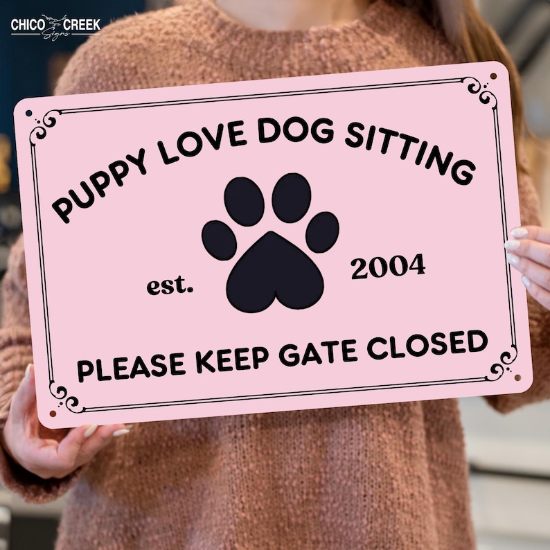 May include: A pink metal sign with black text that reads "PUPPY LOVE DOG SITTING" above a paw print and the year "2004". The bottom of the sign says "PLEASE KEEP GATE CLOSED". Decorative swirls are in each corner.