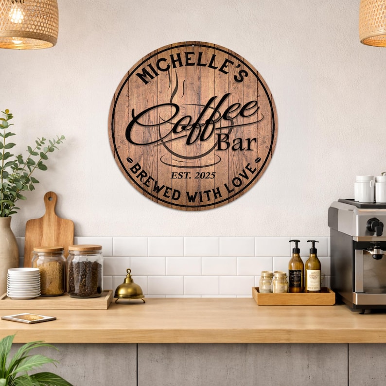 May include: A round wooden sign with the text "Michelle's Coffee Bar" in black script and a coffee cup graphic. The sign also includes "Brewed with Love" and "Est. 2025". The sign is mounted on a white wall above a wooden countertop.