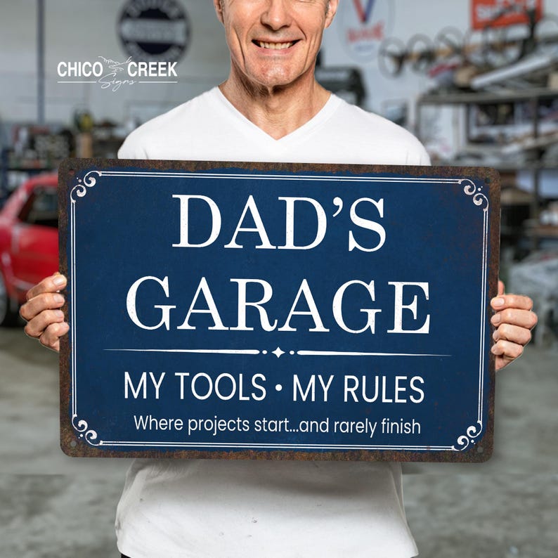Może przedstawiać: Prostokątny niebieski metalowy znak z białym napisem "DAD'S GARAGE". Znak głosi r&oacute;wnież "MY TOOLS &bull; MY RULES" i "Where projects start...and rarely finish". Znak ma ozdobną obw&oacute;dkę.