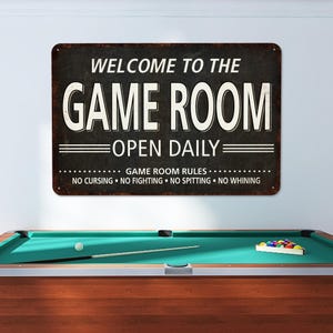 May include: A black and white metal sign with the text "Welcome to the Game Room Open Daily" and the rules "Game Room Rules: No Cursing, No Fighting, No Spitting, No Whining".