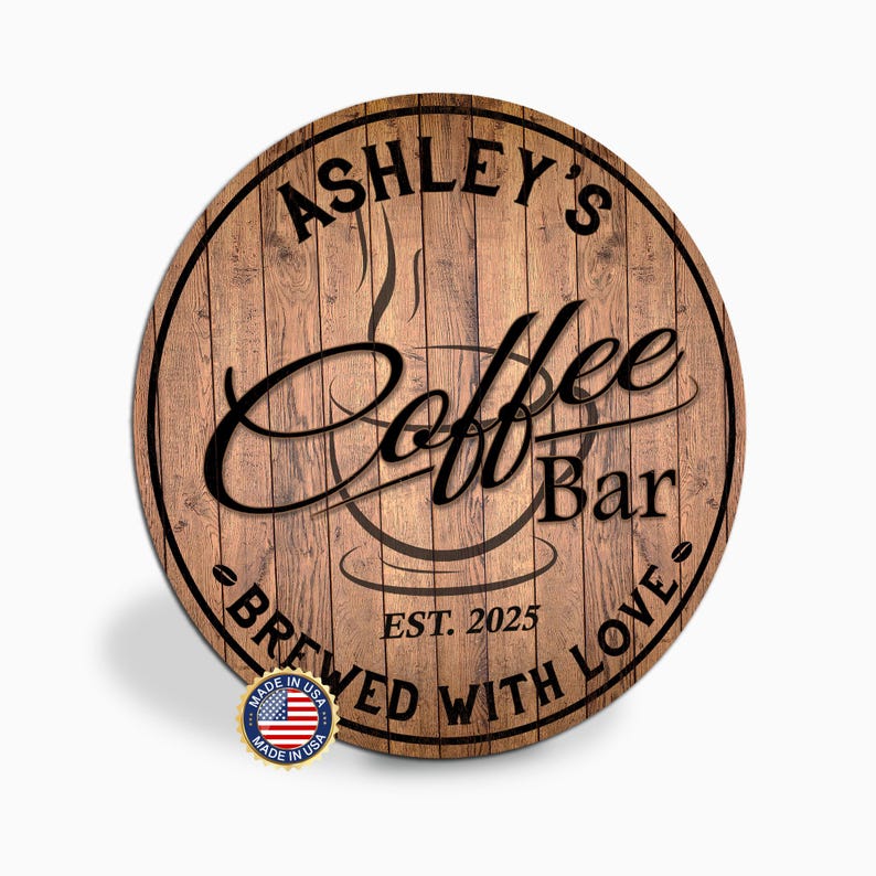May include: Round wooden sign with the text "Ashley's Coffee Bar" in a stylish font. The sign also includes the text "Brewed with Love" and "Est. 2025". A small "Made in USA" emblem is visible at the bottom.