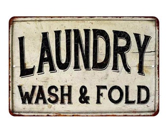 May include: A vintage-style metal sign with a white background and black text that reads "Laundry Wash & Fold". The sign has a distressed, rusty look.