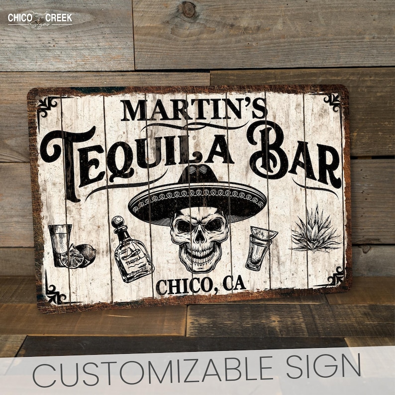 May include: A white wooden sign with black text that reads "Martin's Tequila Bar" with a skull wearing a sombrero, two shot glasses, a bottle of tequila, and a agave plant. The sign also says "Chico, CA" at the bottom.