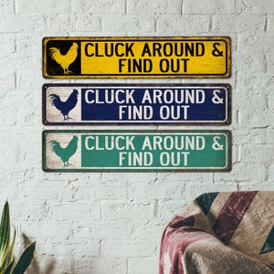 K&ouml;nnte beinhalten: Drei rustikale Holzschilder mit einer Hahnensilhouette und dem Text "CLUCK AROUND & FIND OUT" in Wei&szlig;. Die Schilder sind gelb, blau und gr&uuml;n.