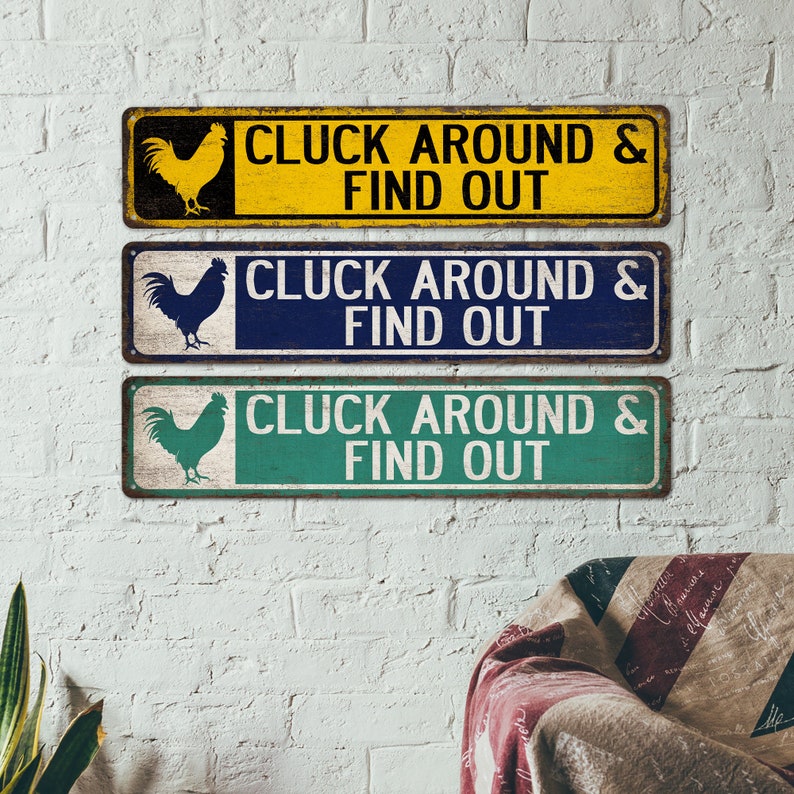 K&ouml;nnte beinhalten: Drei rustikale Holzschilder mit einer Hahnensilhouette und dem Text "CLUCK AROUND & FIND OUT" in Wei&szlig;. Die Schilder sind gelb, blau und gr&uuml;n.