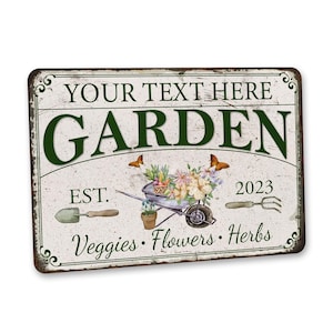 Peut inclure: Une pancarte en m&eacute;tal blanc avec du texte vert qui dit "YOUR TEXT HERE GARDEN EST. 2023 Veggies. Flowers. Herbs". La pancarte pr&eacute;sente une illustration de style vintage d'une brouette remplie de fleurs et de l&eacute;gumes, ainsi que des papillons et des outils de jardinage.