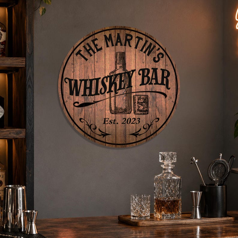 May include: Round wooden sign with the text "THE MARTIN'S WHISKEY BAR" in black, along with a whiskey bottle and glass illustration. The sign is dated "Est. 2023". The sign is mounted on a dark wall.