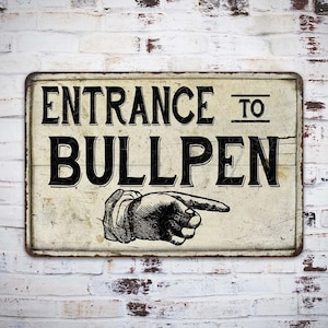May include: A vintage-style metal sign with a white background and black text that reads "Entrance to Bullpen". A black and white illustration of a hand pointing to the right is below the text.