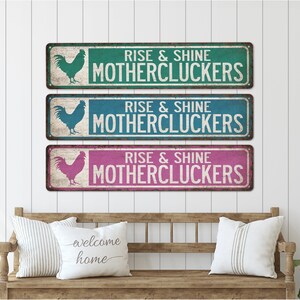 May include: Three rustic metal signs featuring a rooster silhouette and the text "Rise & Shine Mothercluckers" in white. The signs are in teal, blue, and pink.