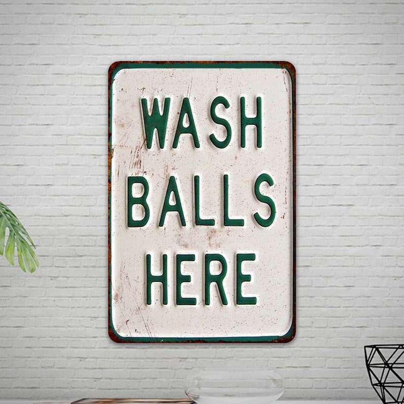 Peut inclure: Une pancarte en m&eacute;tal blanc avec du texte vert qui dit "WASH BALLS HERE". La pancarte a un aspect rustique et vieilli et est accroch&eacute;e &agrave; un mur en briques blanches.