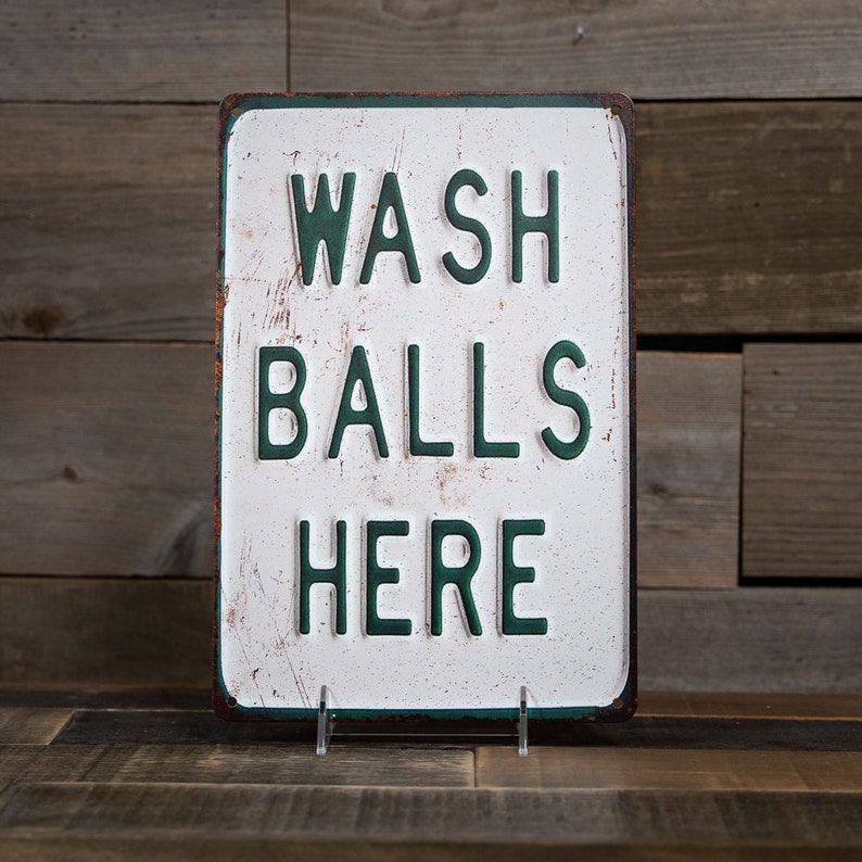 Peut inclure: Un panneau en m&eacute;tal blanc avec du texte vert qui dit "WASH BALLS HERE" sur un fond en bois rustique.